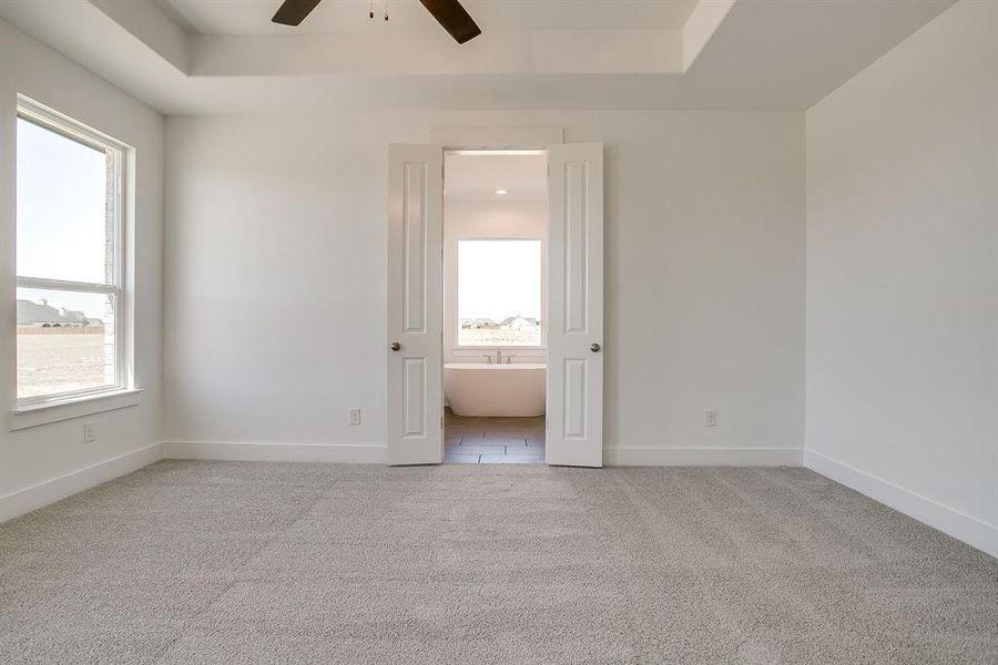 Unfurnished bedroom featuring light colored carpet, a tray ceiling, and ceiling fan Unfurnished bedroom featuring light colored carpet, a tray ceiling, and ceiling fan