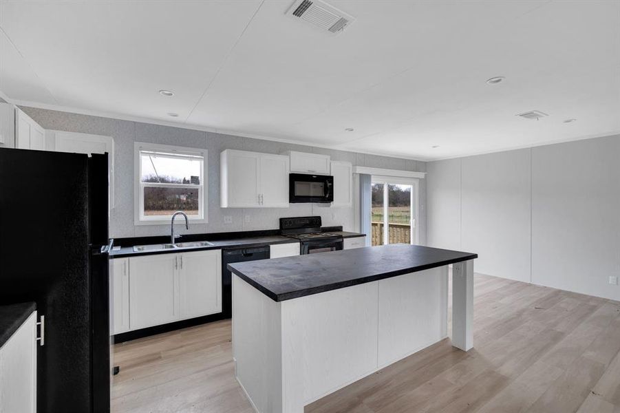 Kitchen with black appliances, healthy amount of natural light, dark countertops, white cabinetry, and crown molding