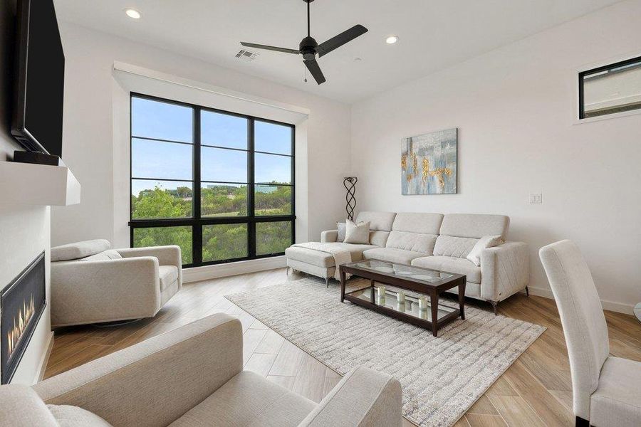 Living space featuring a large black-framed picture window, recessed lighting, a ceiling fan, a built-in electric fireplace, and light wood-finish flooring