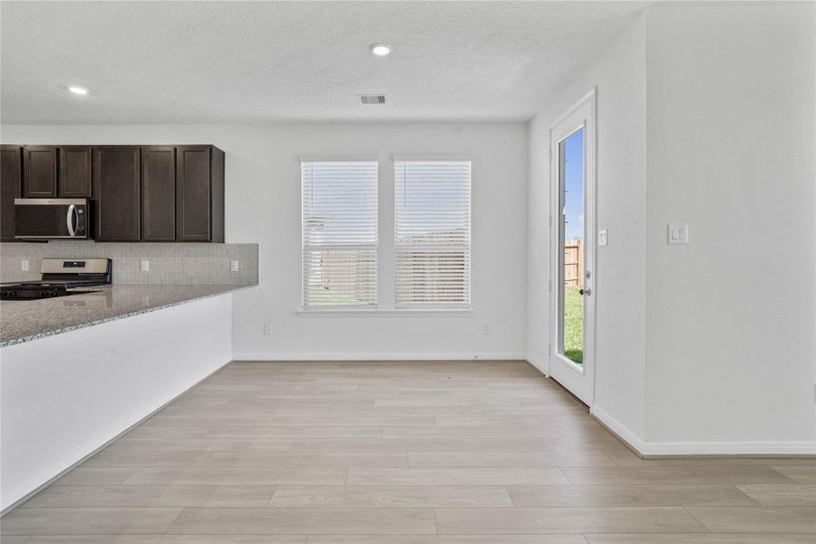 Start your day with a warm cup of coffee and quality time in this charming dining area! Highlights include large windows with blinds, custom neutral paint, vinyl plank flooring, recessed lighting, high ceilings, and a convenient door leading to the rear patio and backyard.