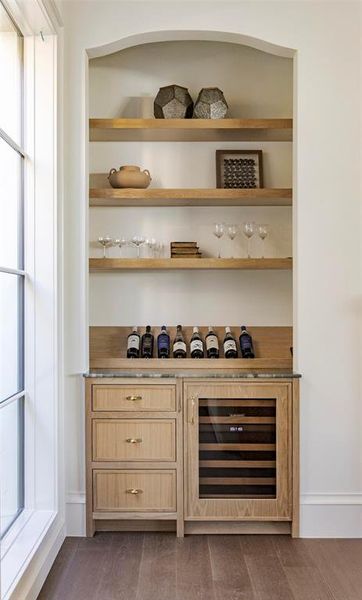 Bar featuring light brown cabinetry, wine cooler, light countertops, dark wood-style floors, and open shelves Bar featuring light brown cabinetry, wine cooler, light countertops, dark wood-style floors, and open shelves