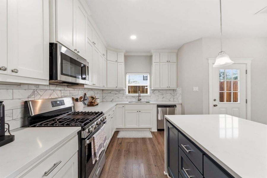 Chef's kitchen features quartz countertops, deep stainless steel sink, stylish ceramic tile backsplash, and custom oversized cabinetry.