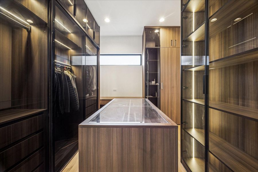 Two walk-in primary closets with custom glass-front shelving and an island.