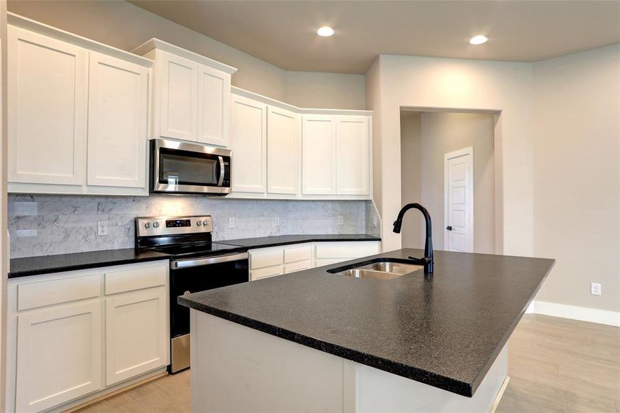 Kitchen with stainless steel appliances, white cabinetry, sink, and a center island with sink