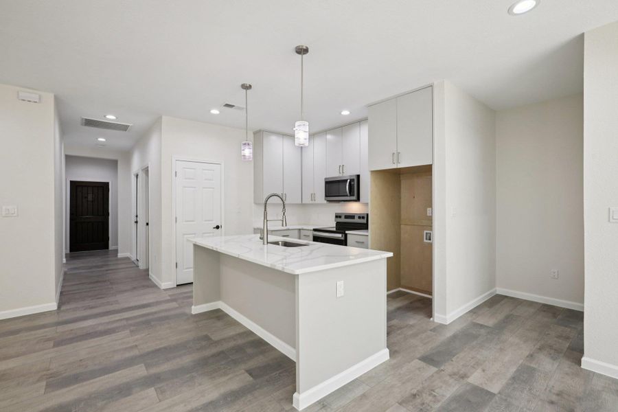 Kitchen with stainless steel appliances, light stone counters, light wood-type laminate flooring, and wood cabinets