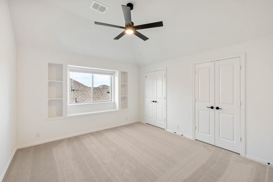 Empty bedroom with carpet, black ceiling fan, built-in shelves, and two white closet doors