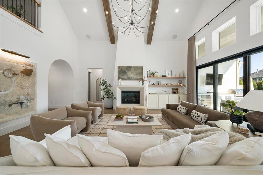 Living room with a large fireplace, light hardwood / wood-style flooring, a high ceiling, and a notable chandelier