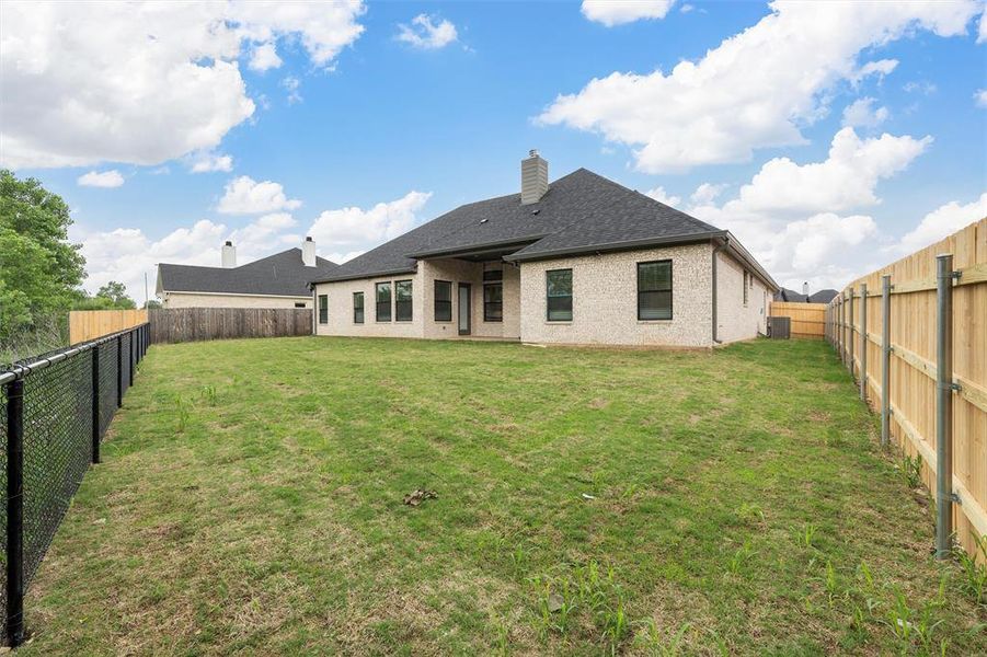 Back of house featuring a fenced backyard, a chimney, and a lawn