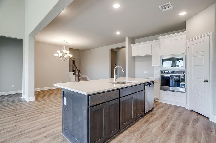 Kitchen with a center island with sink, an inviting chandelier, white cabinets, appliances with stainless steel finishes, and sink Kitchen with a center island with sink, an inviting chandelier, white cabinets, appliances with stainless steel finishes, and sink