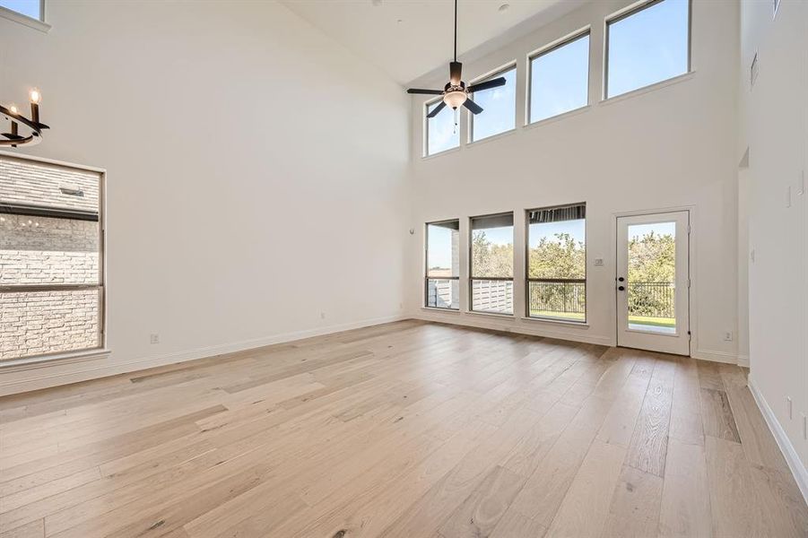 Unfurnished living room featuring ceiling fan with notable chandelier, light hardwood / wood-style floors, and high vaulted ceiling