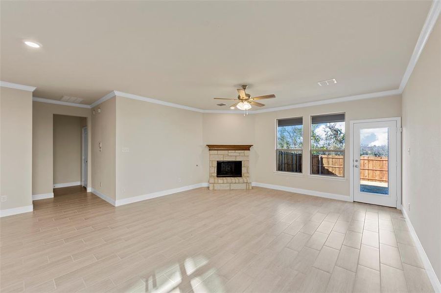 Unfurnished living room with a stone fireplace, ceiling fan, and ornamental molding