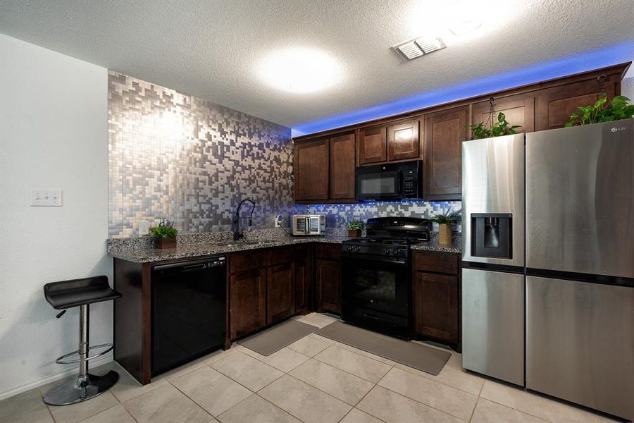 Kitchen featuring black appliances, dark stone counters, decorative backsplash, and sink