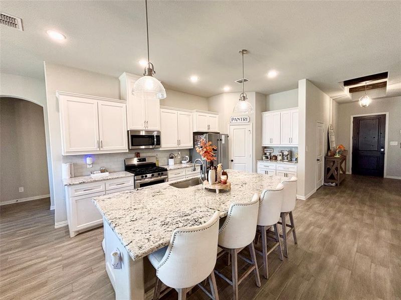 Kitchen with a kitchen bar, white cabinetry, appliances with stainless steel finishes, arched walkways, and light wood-style floors Kitchen with a kitchen bar, white cabinetry, appliances with stainless steel finishes, arched walkways, and light wood-style floors