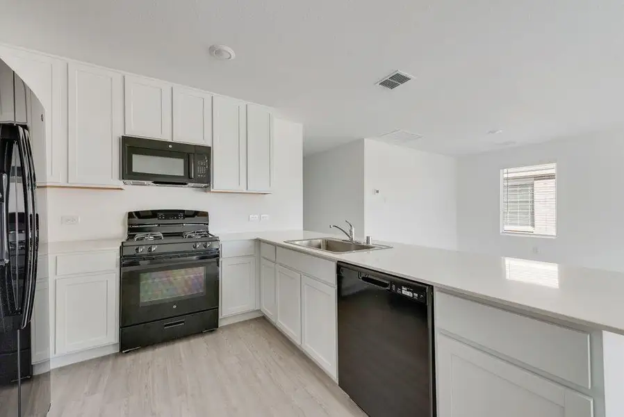 Kitchen featuring black appliances, light wood finished floors, white cabinetry, a peninsula, and light stone countertops