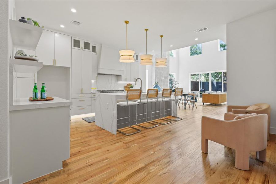 Kitchen with white cabinetry, light hardwood / wood-style flooring, a center island with sink, and premium range hood