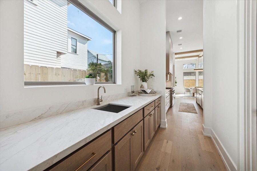 The butler’s pantry features an undermount stainless steel sink, ample storage, and a spacious countertop for prep work, with a walk-in pantry and built-ins conveniently located across from the sink.