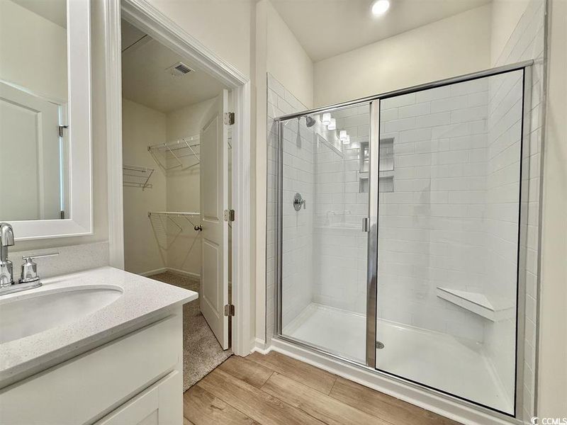 Full bath featuring a shower stall, vanity, light wood-style floors, and a walk in closet Full bath featuring a shower stall, vanity, light wood-style floors, and a walk in closet