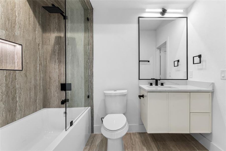 Sleek bathroom featuring a floating vanity with a stone countertop, a rectangular mirror with a black frame, and a tub-shower combination with a glass panel and matte black fixtures Sleek bathroom featuring a floating vanity with a stone countertop, a rectangular mirror with a black frame, and a tub-shower combination with a glass panel and matte black fixtures