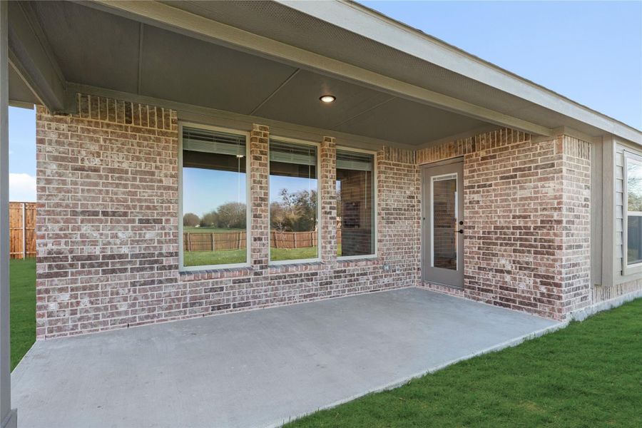Covered back patio with concrete slab, brick exterior, large windows, and rear entry door overlooking grassy yard Covered back patio with concrete slab, brick exterior, large windows, and rear entry door overlooking grassy yard