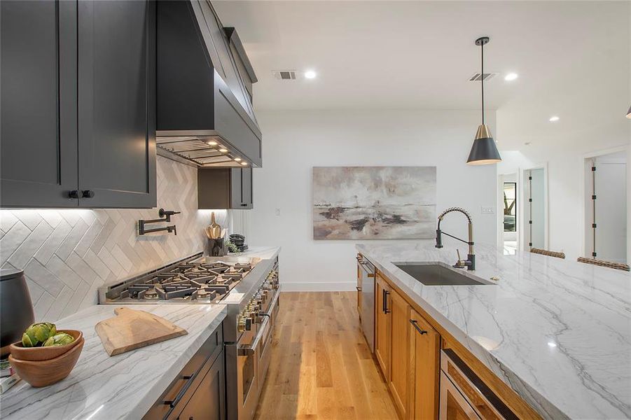 Kitchen featuring light stone counters, wall chimney exhaust hood, stainless steel appliances, sink, and hanging light fixtures