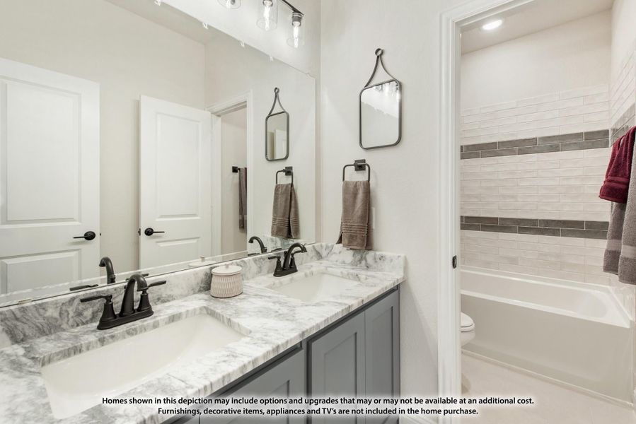Bathroom with double vanity, gray cabinets, marble countertops, and tiled bathtub surround