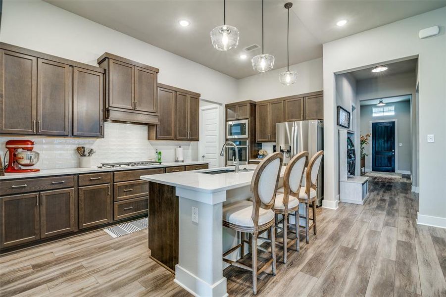 Kitchen featuring a breakfast bar area, pendant lighting, stainless steel appliances, a kitchen island with sink, and sink