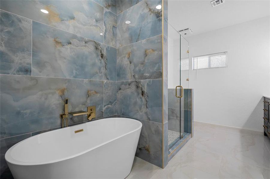 Freestanding soaking tub with gold-finish fixtures and blue-hued marbled wall tiling Freestanding soaking tub with gold-finish fixtures and blue-hued marbled wall tiling