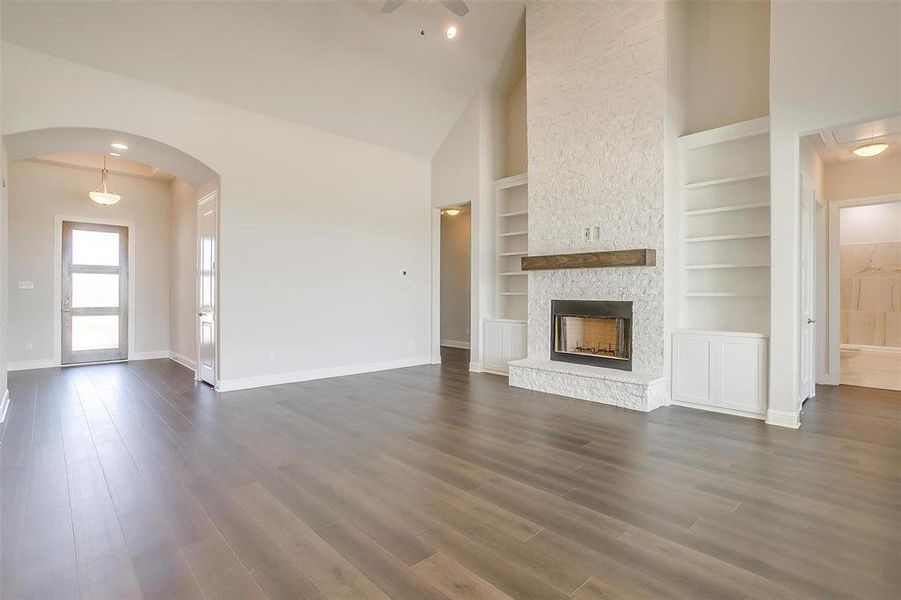 Unfurnished living room featuring dark wood-type flooring, built in shelves, ceiling fan, a fireplace, and high vaulted ceiling