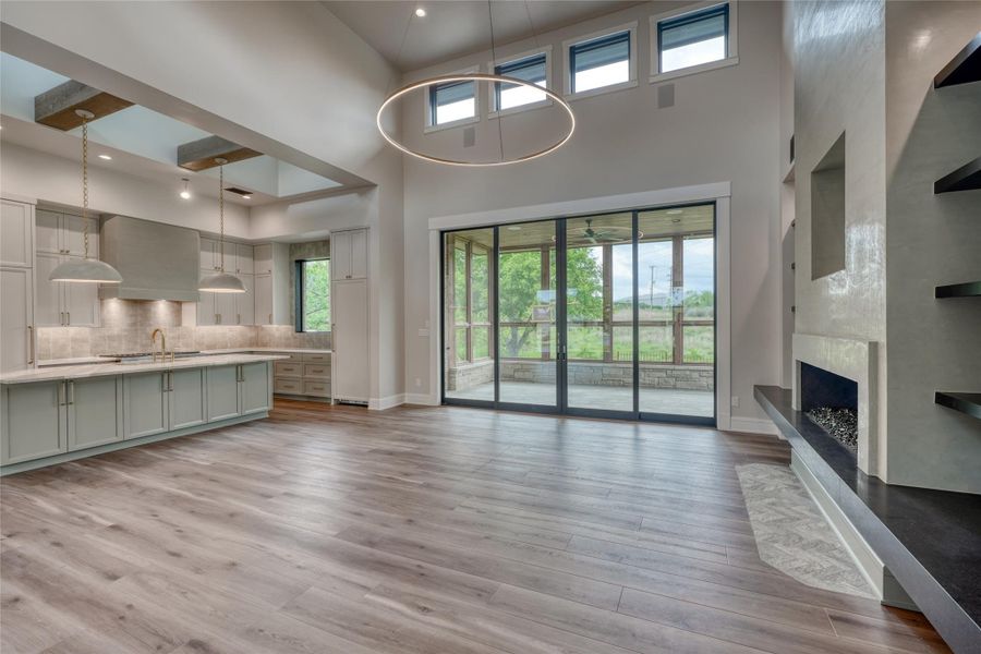 Unfurnished living room featuring a high ceiling, baseboards, a fireplace with raised hearth, light wood-style floors, and a sink