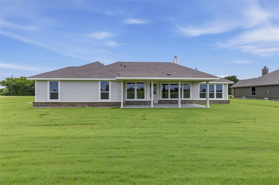 Expansive rear facade featuring a covered patio with supporting columns, large windows, light-colored siding, and a stone-finish foundation Expansive rear facade featuring a covered patio with supporting columns, large windows, light-colored siding, and a stone-finish foundation