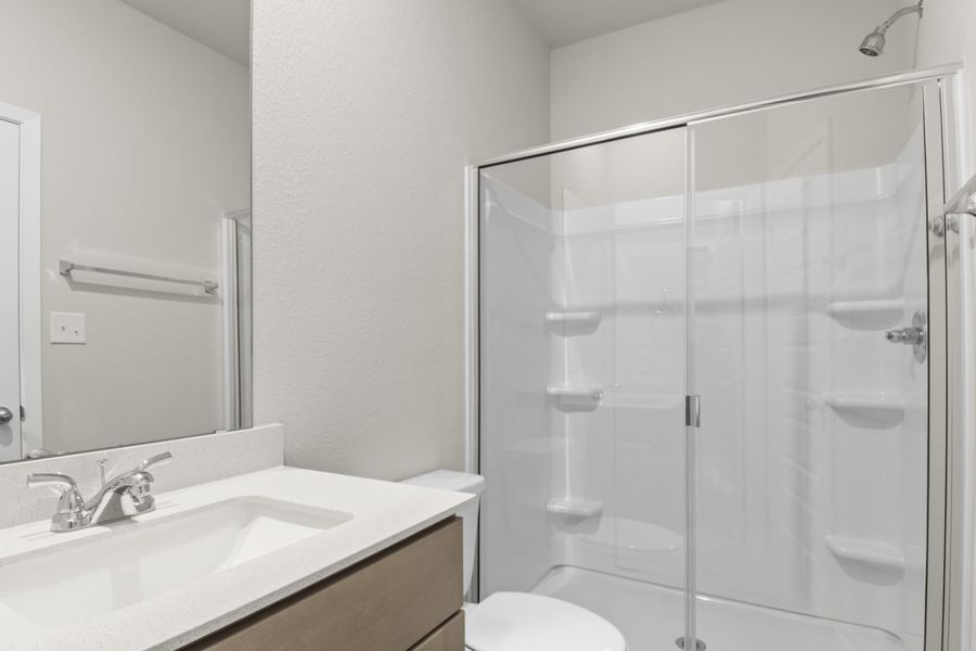 Image of a primary bathroom with light brown cabinets and a white countertop with a mirror and walk-in shower