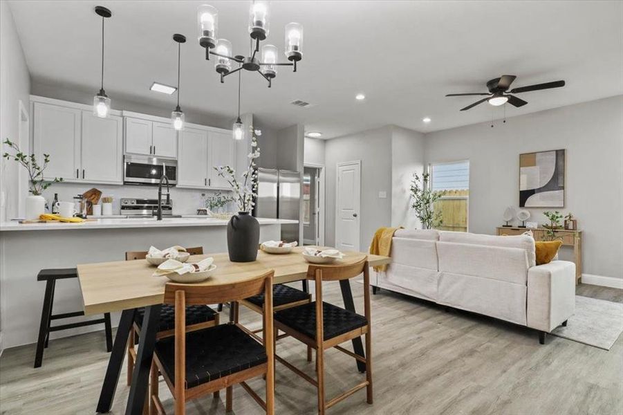 Dining room with ceiling fan with notable chandelier and light hardwood / wood-style floors