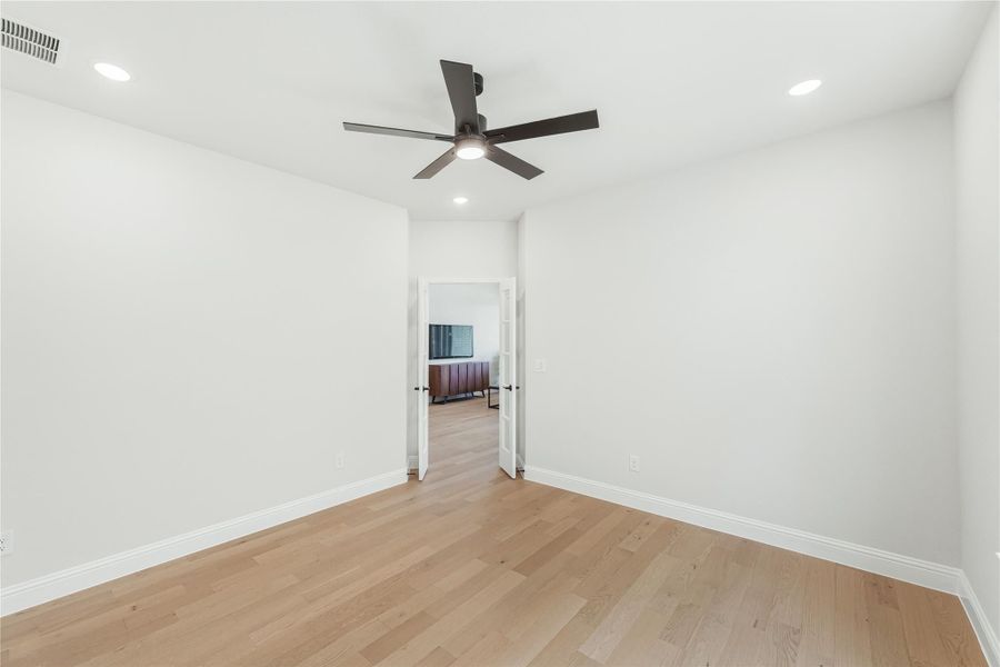 Empty bedroom with light hardwood floors, ceiling fan, and open doorway to adjoining room