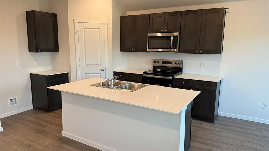 Kitchen featuring stainless steel appliances, dark wood finish cabinetry, a center island with sink, and dark wood finished floors
