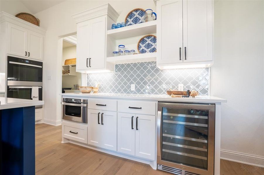 Kitchen featuring wine cooler, white cabinetry, double oven, open shelves, and light wood-style flooring Kitchen featuring wine cooler, white cabinetry, double oven, open shelves, and light wood-style flooring