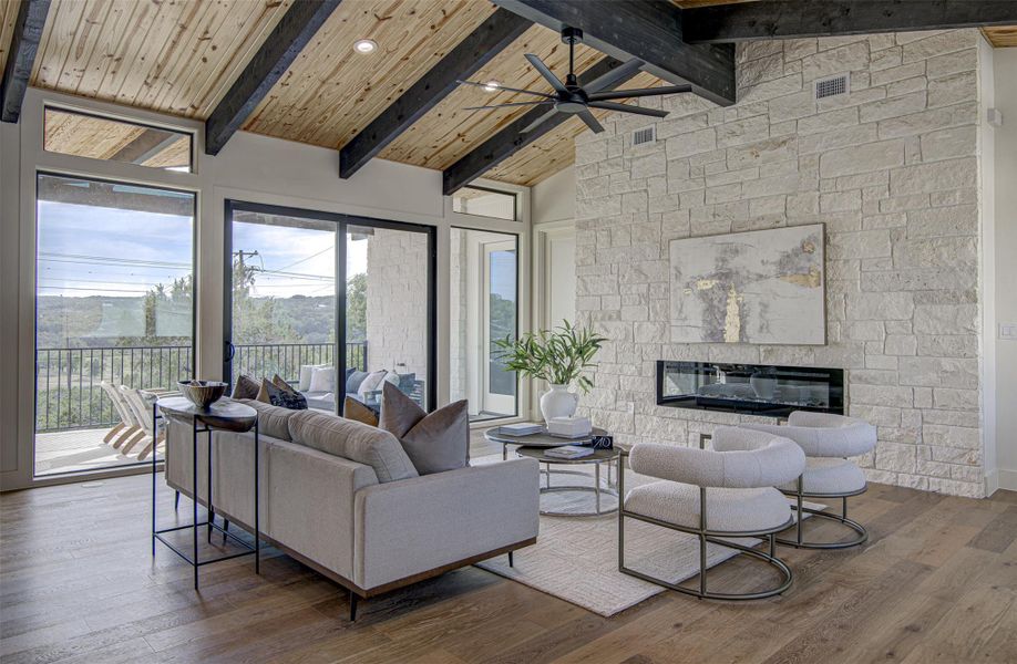 Living room with ceiling fan, beam ceiling, plenty of natural light, wood finished floors, and a stone fireplace Living room with ceiling fan, beam ceiling, plenty of natural light, wood finished floors, and a stone fireplace