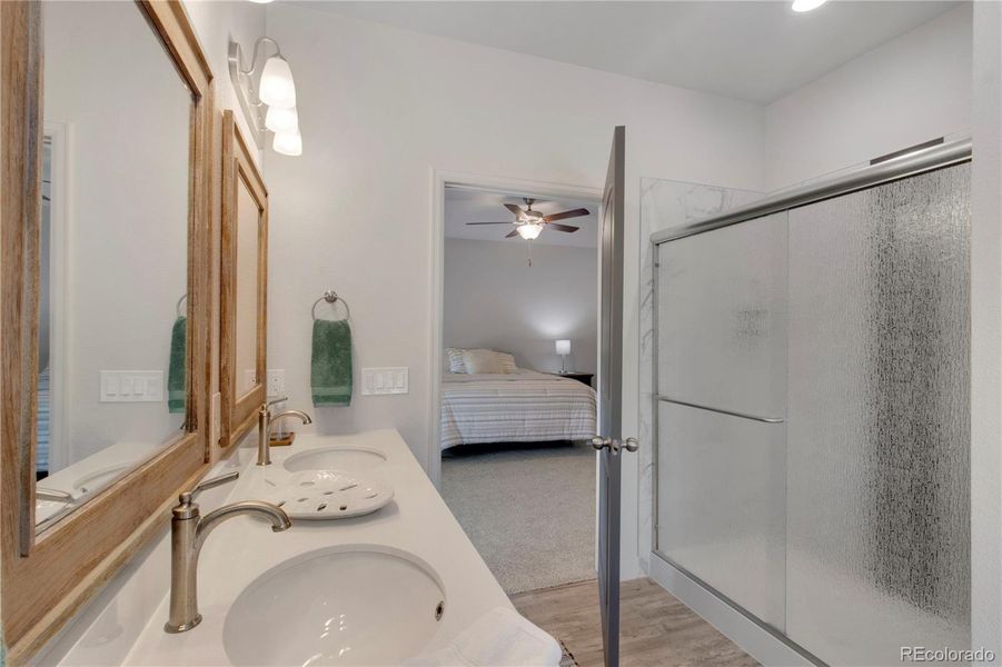 Bathroom featuring a garden tub, double vanity, a shower with door, and wood finished floors