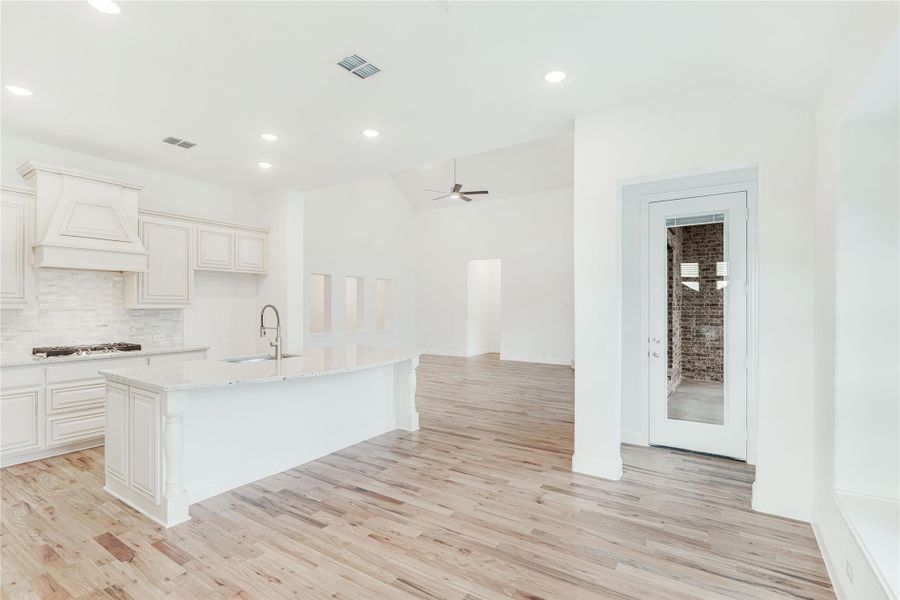 Open kitchen with white cabinets, large island, tile backsplash, and light hardwood floors opening to living area