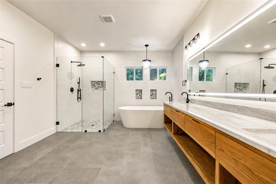 Spacious and elegant Primary bathroom with a modern glass-enclosed shower, freestanding tub, dual sinks, and sleek fixtures, complemented by a large mirror and contemporary lighting.