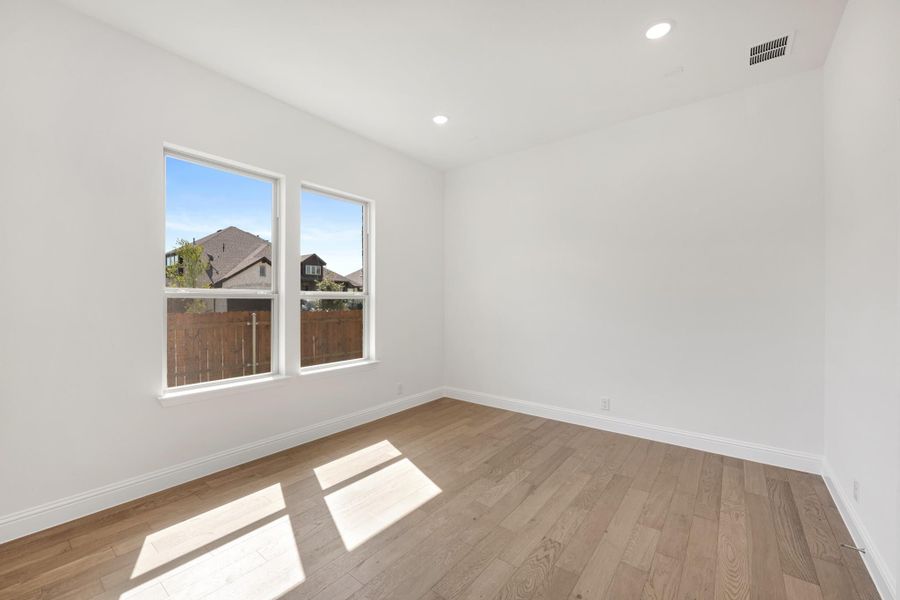 Empty room with white walls, hardwood floors, and two windows overlooking neighboring homes