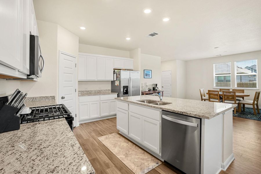 A contemporary kitchen features bright white cabinetry and granite countertops, complemented by recessed lighting and durable wood flooring.