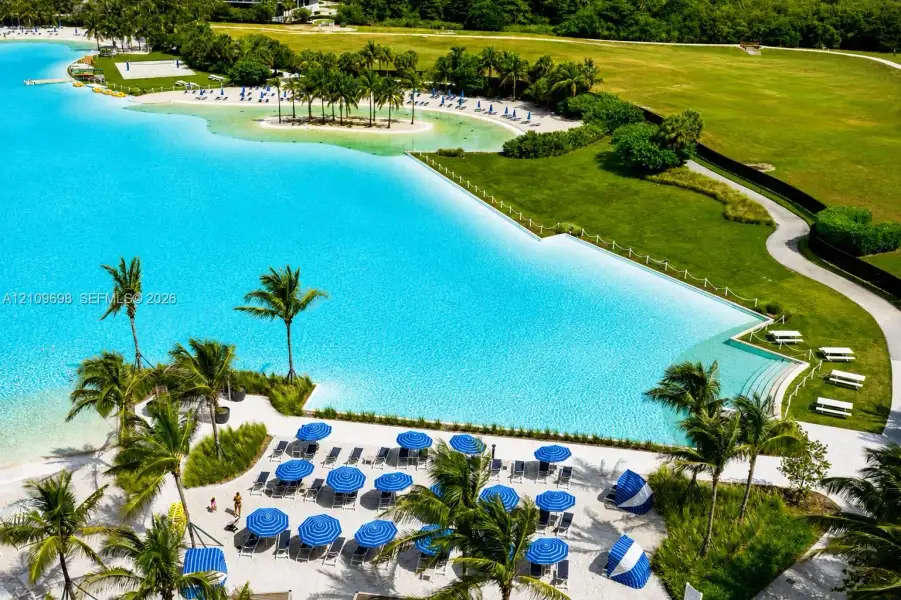 Man-made lagoon featuring a white sand beach, extensive perimeter landscaping, walking paths, and concrete terraced stairs leading to the water