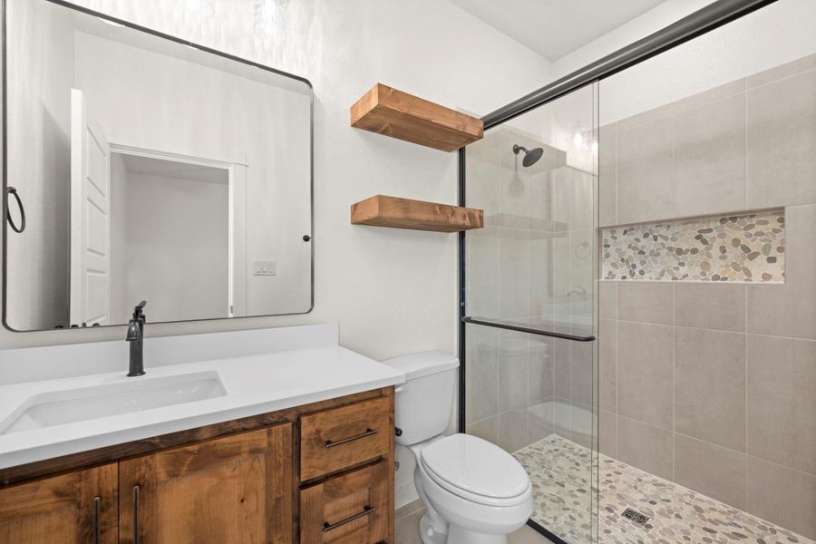 A well-appointed bath features a spacious glass-enclosed shower and a handsome vanity with floating shelves.