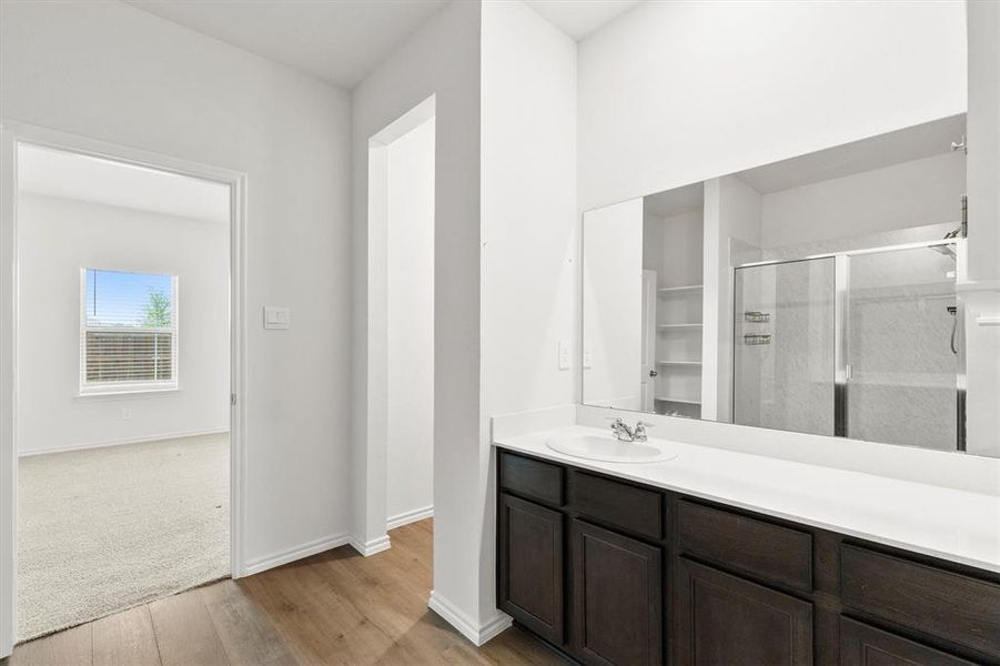 Bathroom vanity featuring a single-basin sink, expansive mirror, dark wood-finish cabinetry, and solid surface countertop