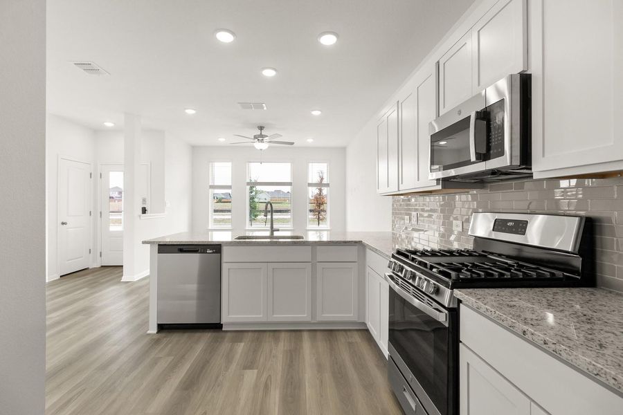 Kitchen with stainless steel appliances, a peninsula, backsplash, light stone counters, and light wood-type flooring