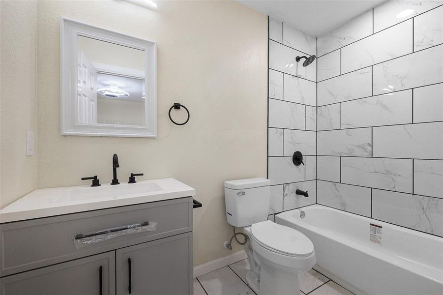 Full bathroom with toilet, tile patterned floors, tiled shower / bath combo, and vanity