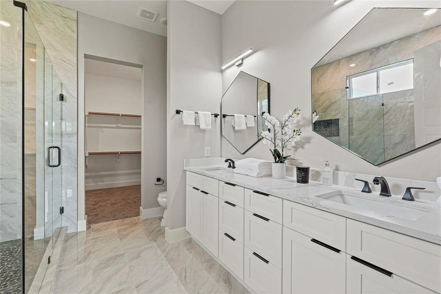 Bathroom with a stall shower, double vanity, marble finish flooring, and a walk in closet