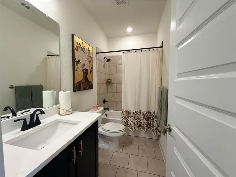 Bathroom featuring a black vanity with a white countertop and integrated sink, matte black faucet, and a large wall mirror Bathroom featuring a black vanity with a white countertop and integrated sink, matte black faucet, and a large wall mirror