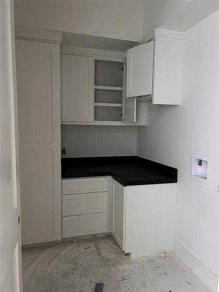 Utility room with beige and black checkered flooring. Plenty of storage space and hanging rack.