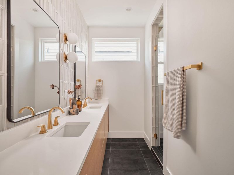 Full bathroom featuring double vanity, dark tile patterned floors, healthy amount of natural light, and a shower with shower door